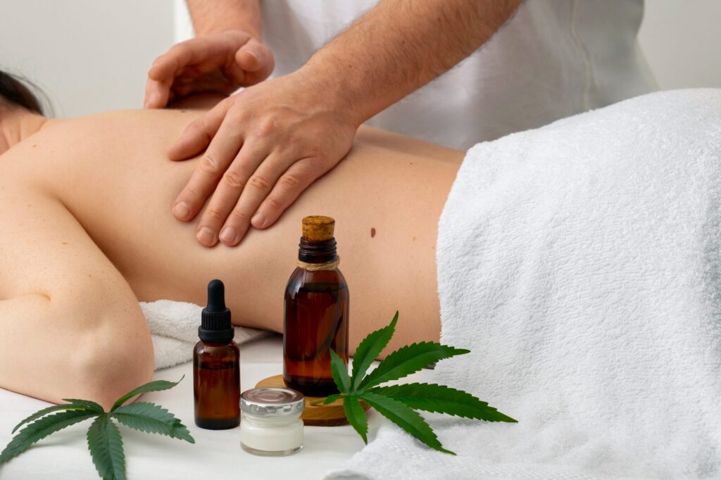 Close-up of therapeutic massage on back using aromatherapy oils with hemp leaves, dropper bottles, and cream for natural exhaustion relief.