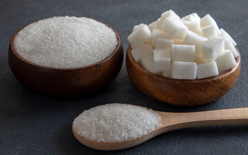 Bowls of granulated white sugar and sugar cubes with spoon, illustrating effects of too much sugar on body and health tips.