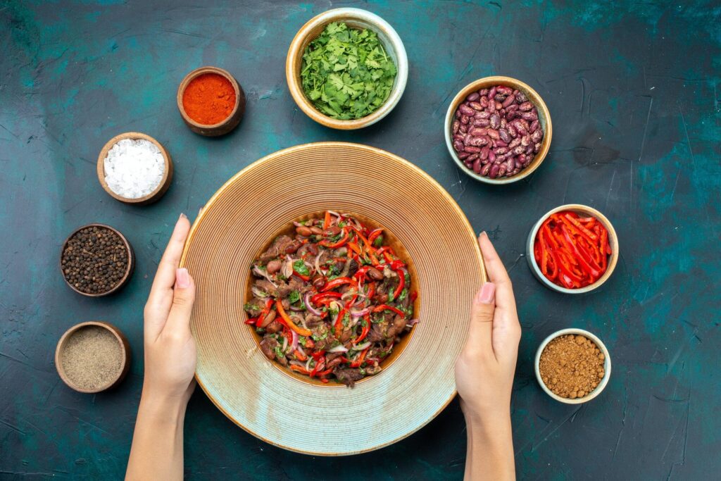 Hands holding large bowl of vibrant Rajma salad with kidney beans, red bell peppers, onions, and fresh cilantro, surrounded by spices for lymphatic health.