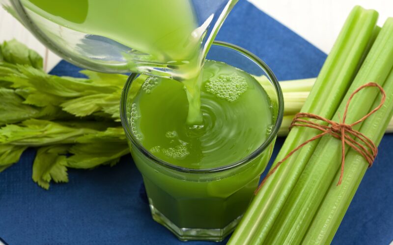 Pouring fresh green celery juice into glass with stalks, for natural lymphatic detox and inflammation reduction.