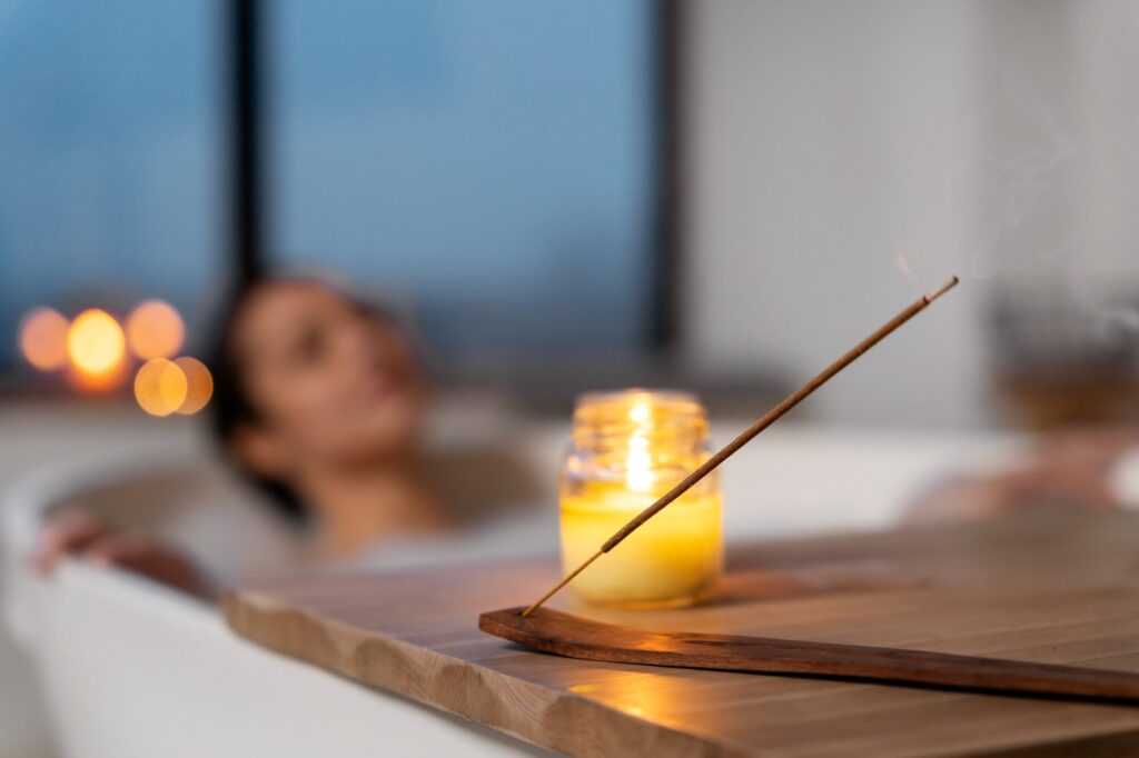 Person in bathtub enjoying aromatherapy with burning incense stick, lit candle, and calming spa ambiance to help reduce pain naturally.