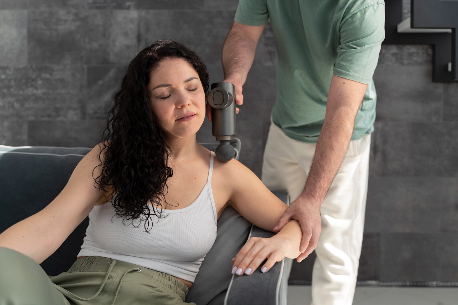 Woman receiving percussion massage therapy on her shoulder for chronic pain relief at the San Diego neuromuscular massage clinic