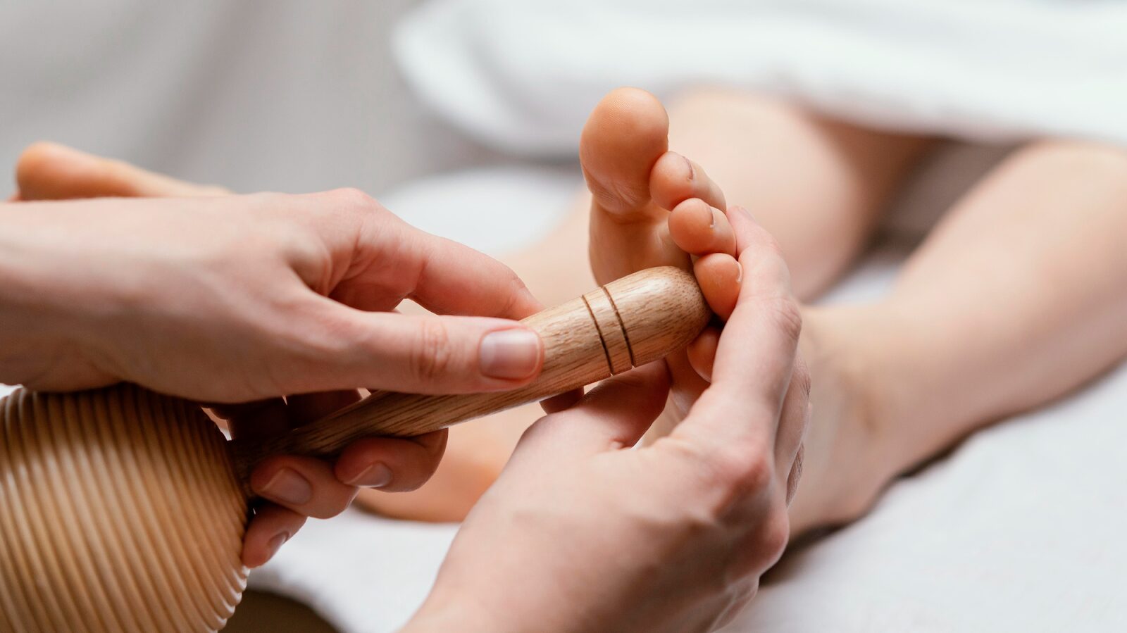 Reflexology therapist using a wooden massage tool on the client's foot pressure points for natural pain relief in San Diego
