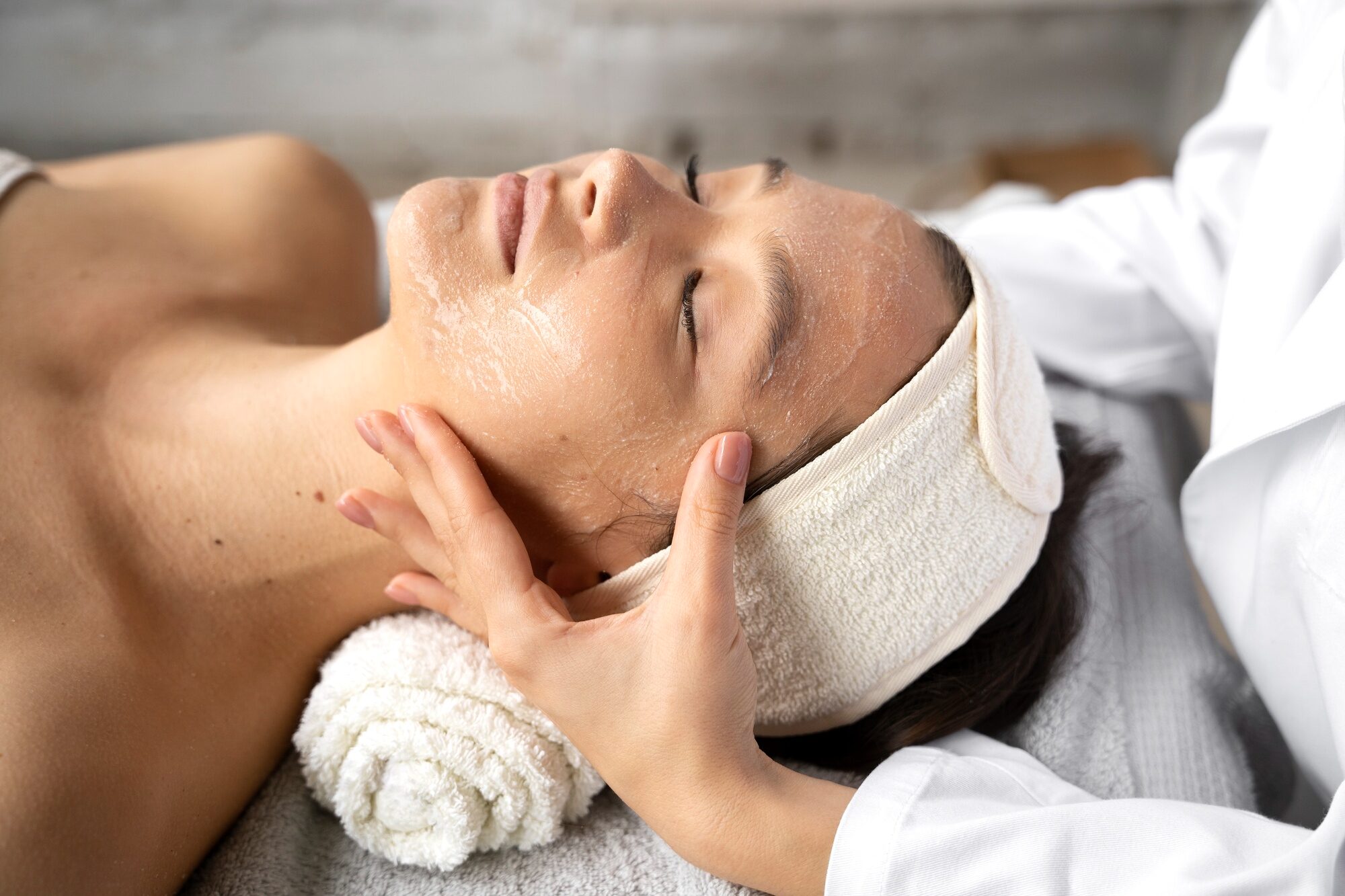 Professional esthetician performing detoxifying facial massage treatment with cleansing mask at San Diego wellness spa 