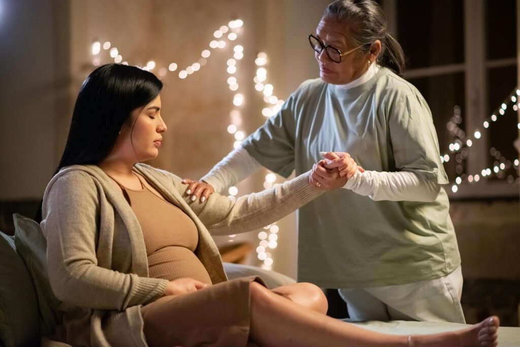 A therapist at Beauty Kliniek provides supportive hand and shoulder touch to a pregnant woman for relaxation.